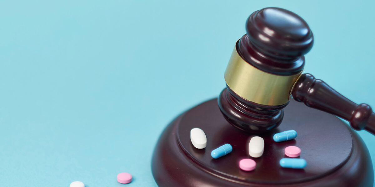 Elmiron Lawsuit Claims Vision Loss featured image showing a gavel slamming on top of multi colored drugs in the form of pills