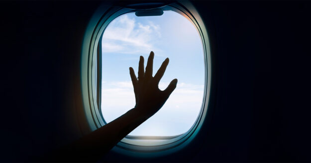 Sexually Assaulted On A Plane You Have Rights hand against the dark pane of a window on an airplane