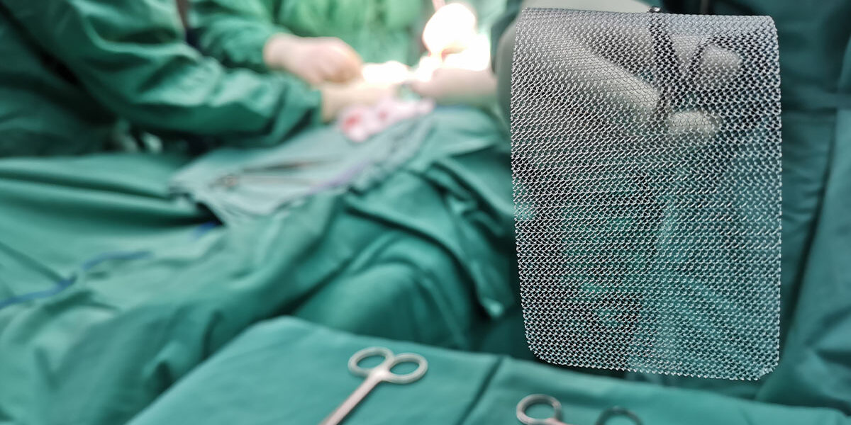 Doctor holding a hernia mesh with forceps during surgery